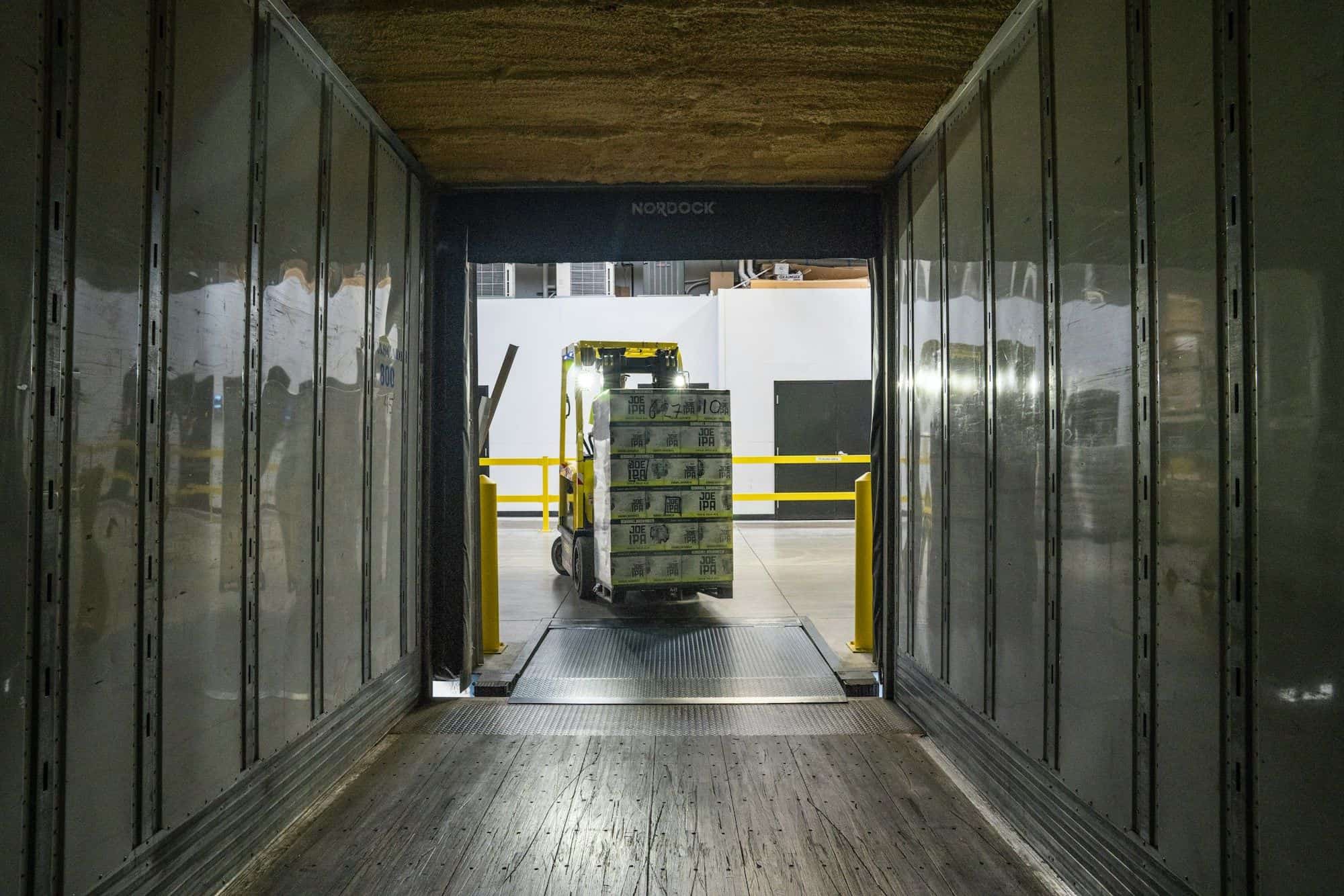 Forklift loading a pallet into a container trailer at a warehouse dock