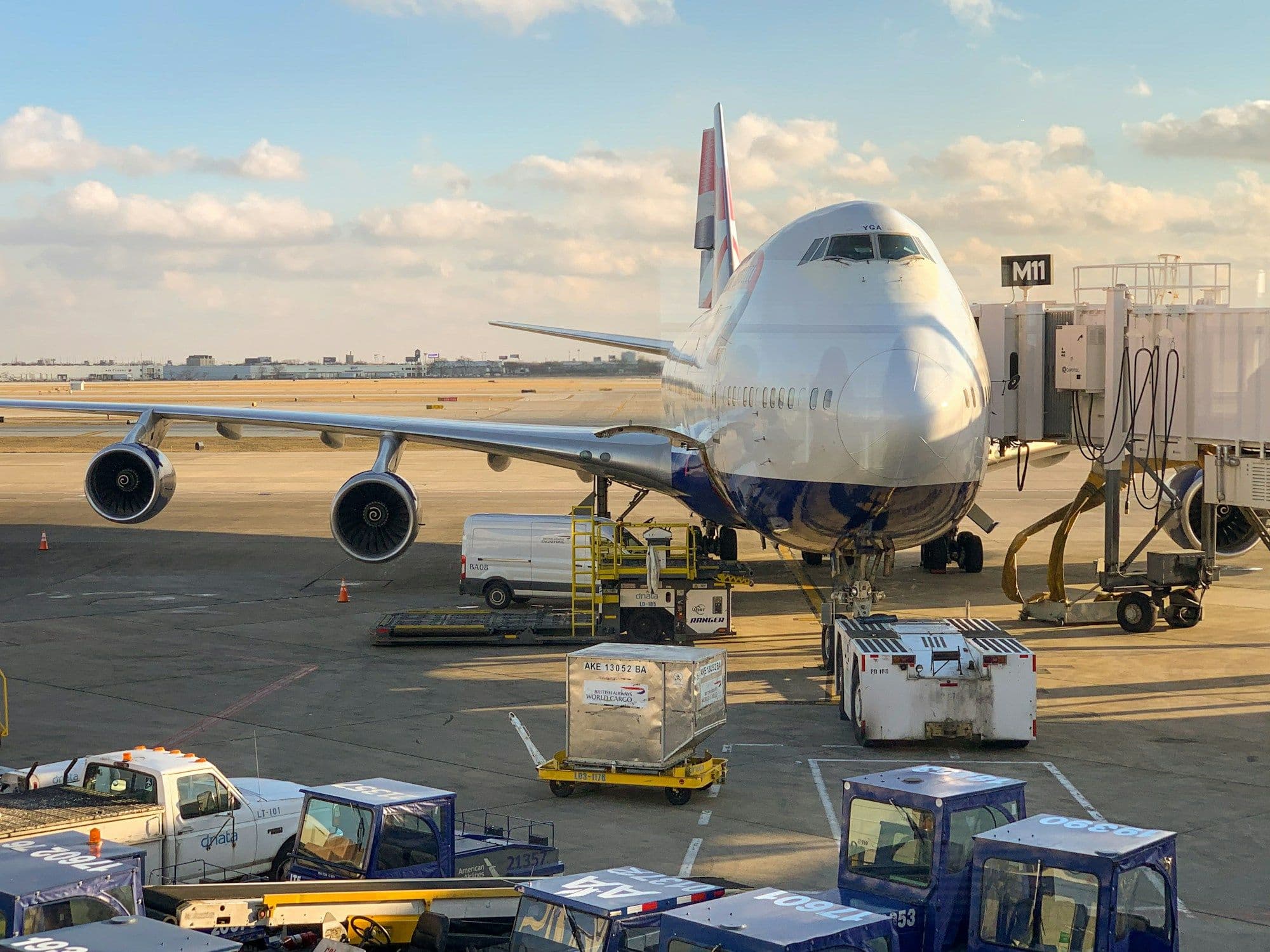 Wide-body aircraft at the gate being serviced with cargo dollies at golden hour
