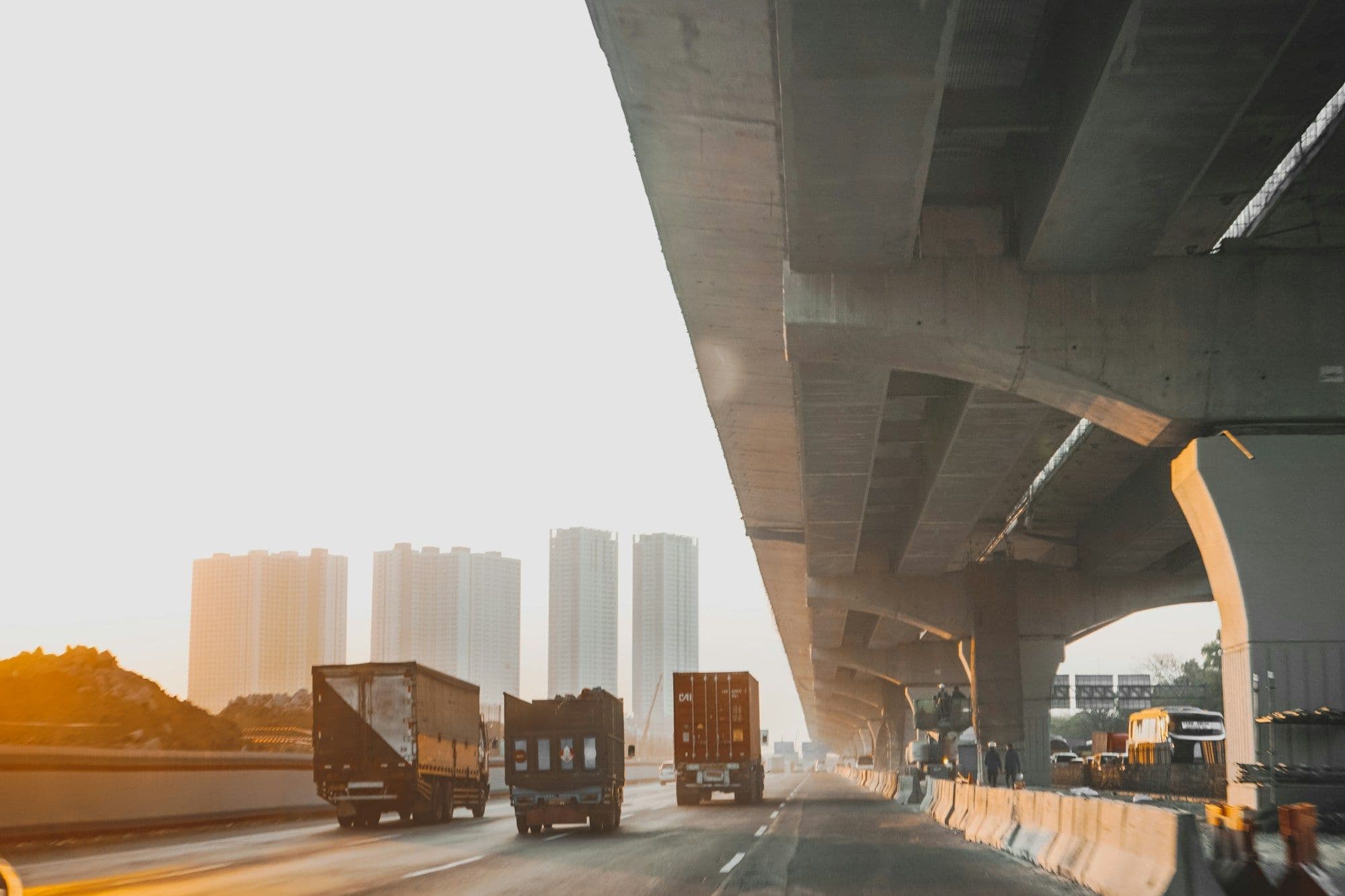 Goods trucks driving under a city flyover at sunrise