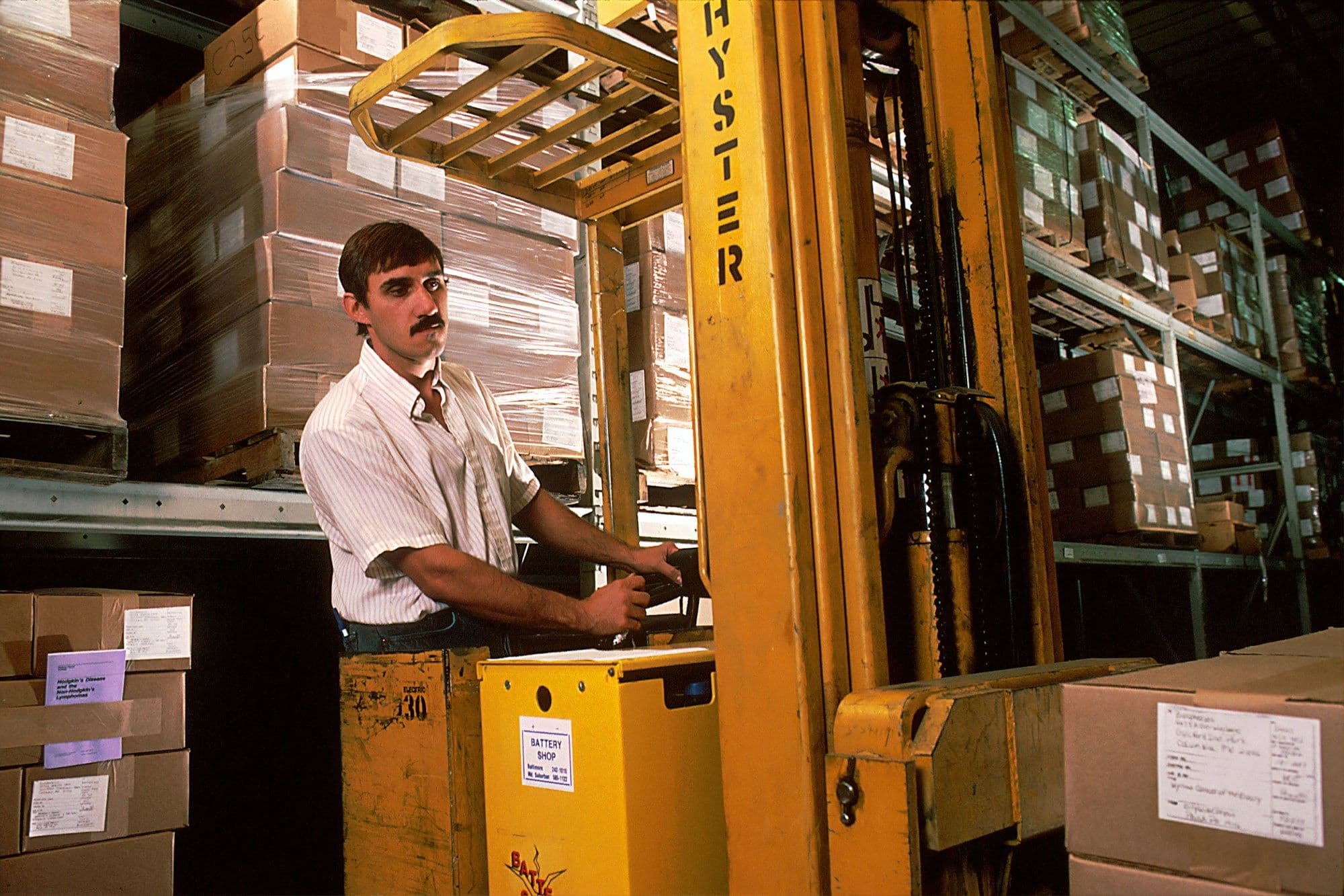 Warehouse operator driving a forklift between shelves of cartons